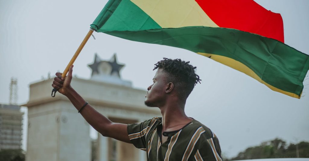 african-male-with-dreadlocks-raising-flag-of-ghana-country-with-colorful-stripes-while-looking-away