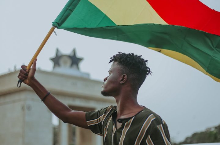 african-male-with-dreadlocks-raising-flag-of-ghana-country-with-colorful-stripes-while-looking-away