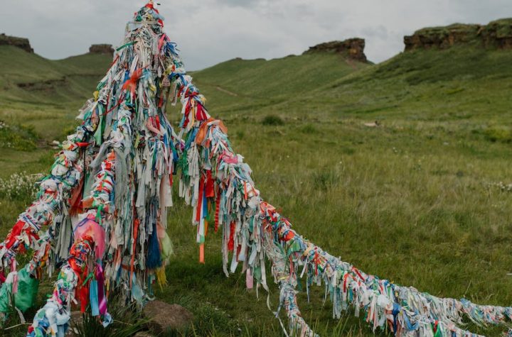 tibetan-bright-flags-located-in-field-with-fresh-green-grass-and-rocky-formations-under-cloudy-sky-2